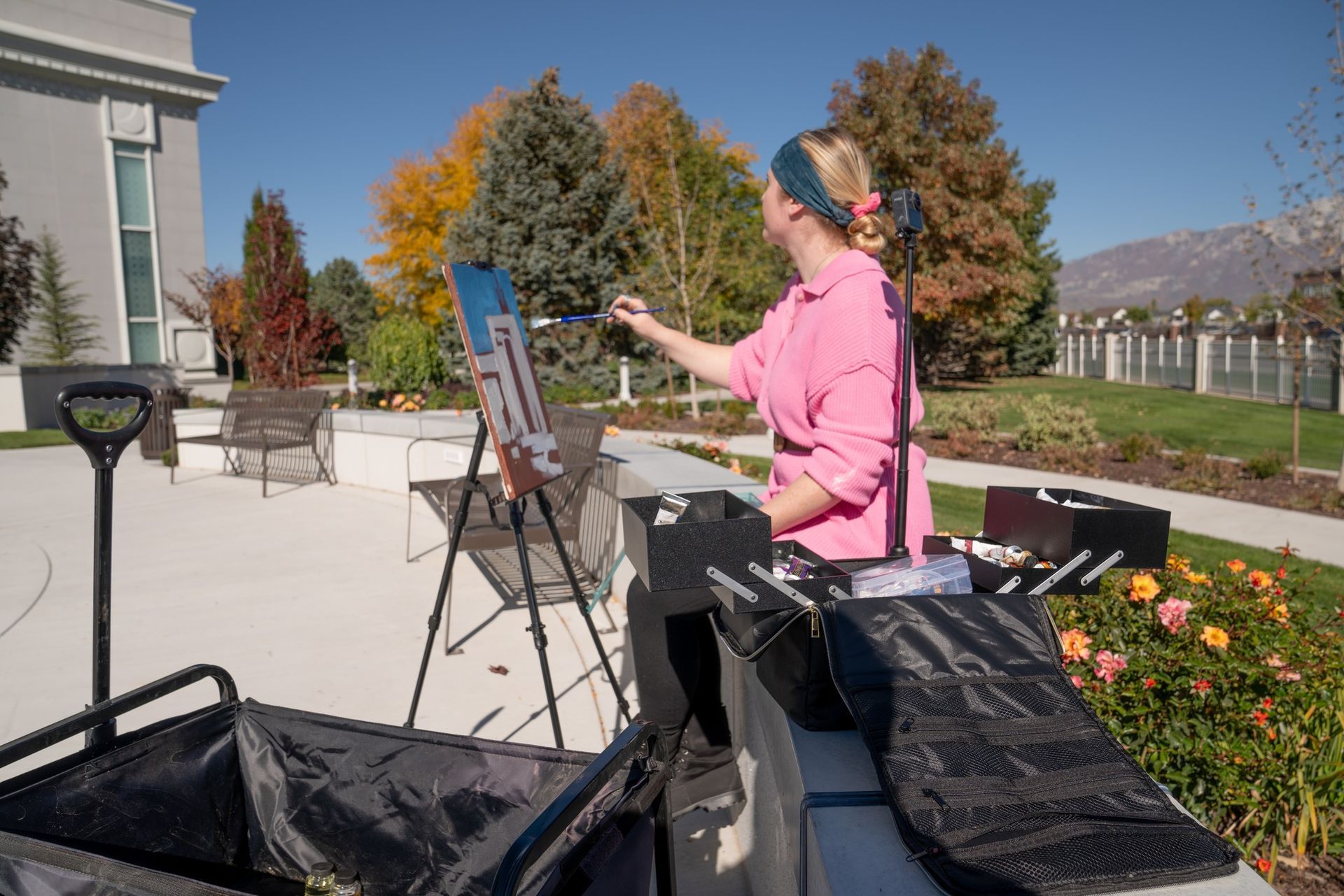 A woman in a pink shirt is painting on an easel outside