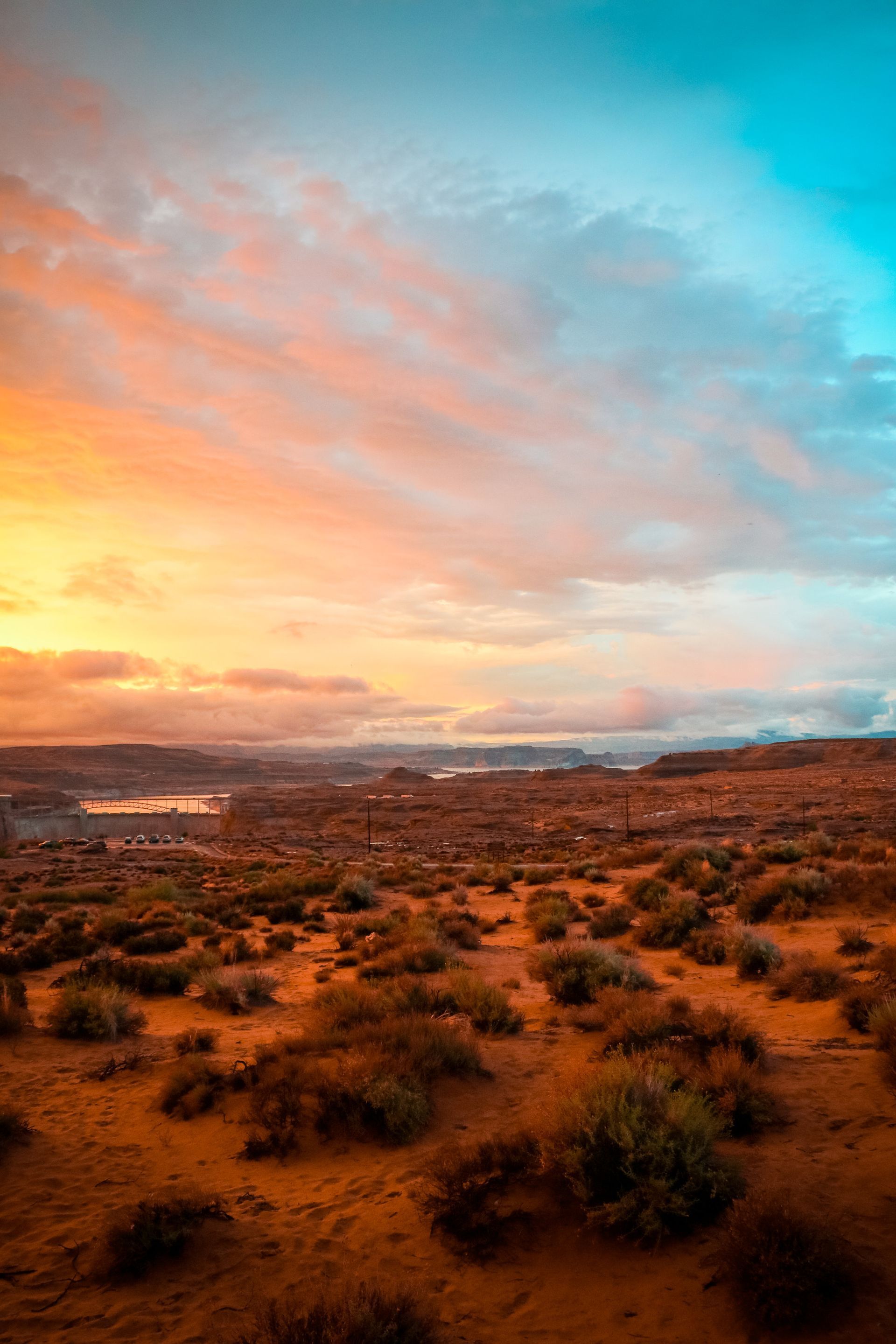 A sunset over a desert landscape with a lake in the distance.