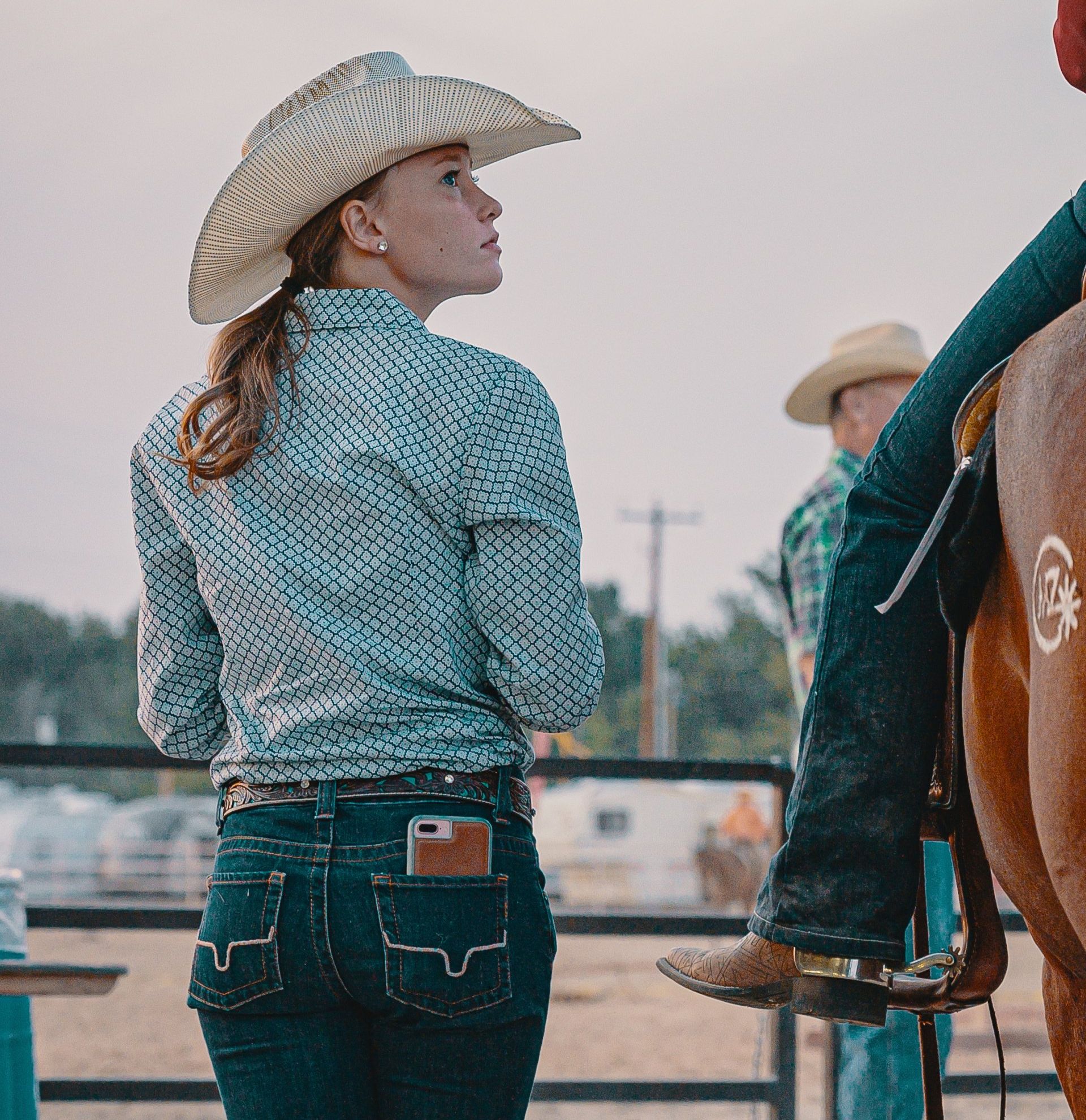 A woman wearing a cowboy hat is standing next to a man riding a horse