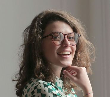 A woman wearing glasses and a green and white shirt is smiling.