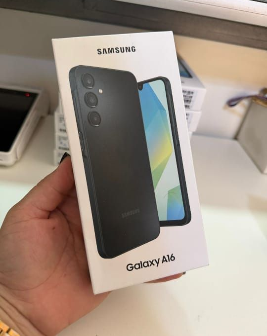 Una mano sosteniendo una caja de teléfono Samsung Galaxy A16, blanca con la imagen del teléfono, sobre un fondo claro.