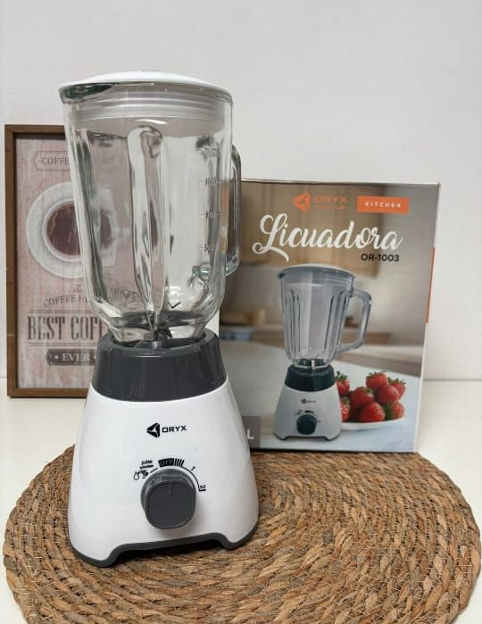 Licuadora blanca con jarra de vidrio, al lado de su caja sobre una estera tejida.