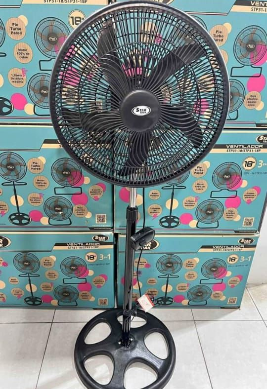 Abanico de pie de color negro delante de varias cajas color verde azulado del mismo producto.