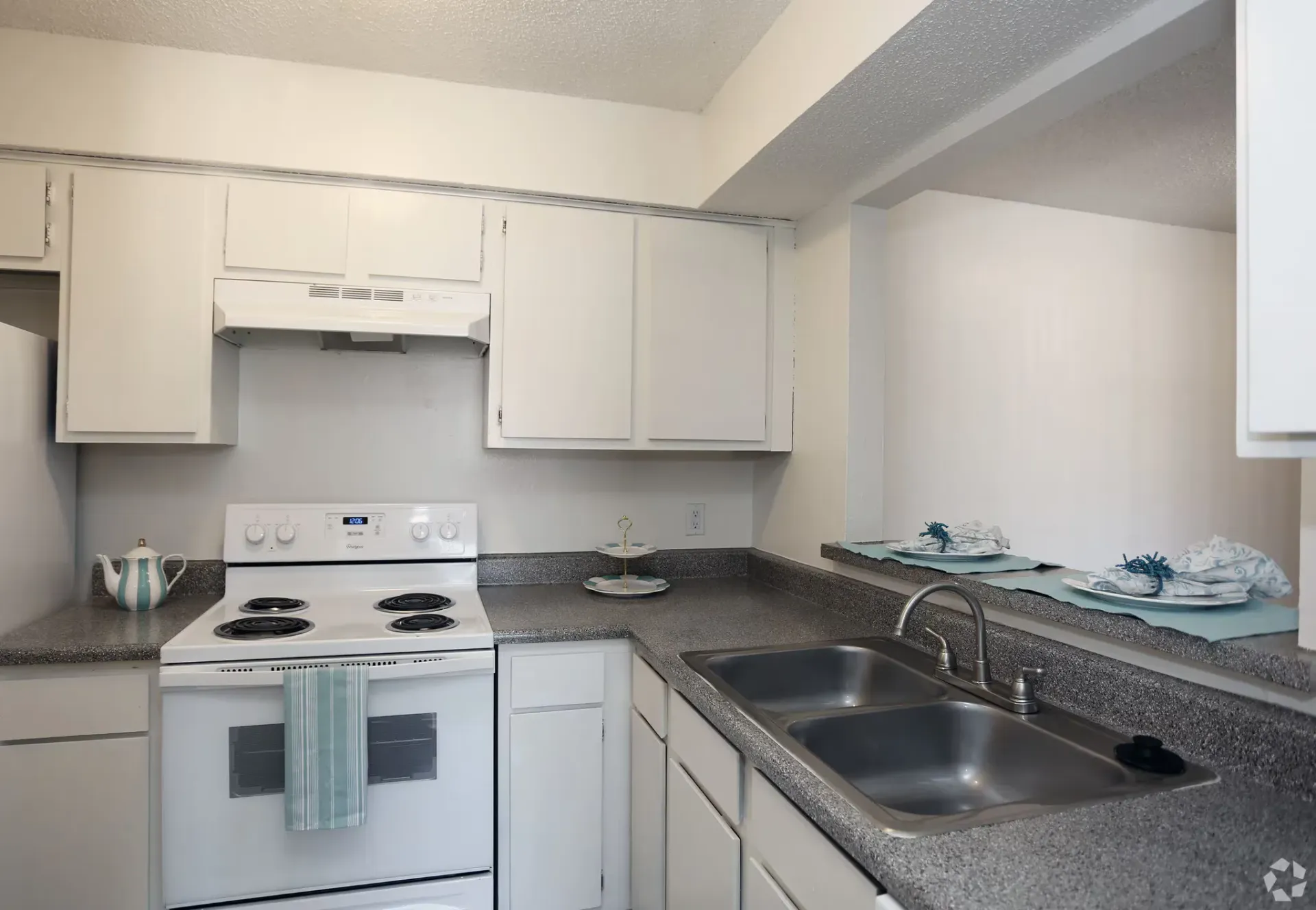 White kitchen with stove, cabinets, sink, and speckled countertops.