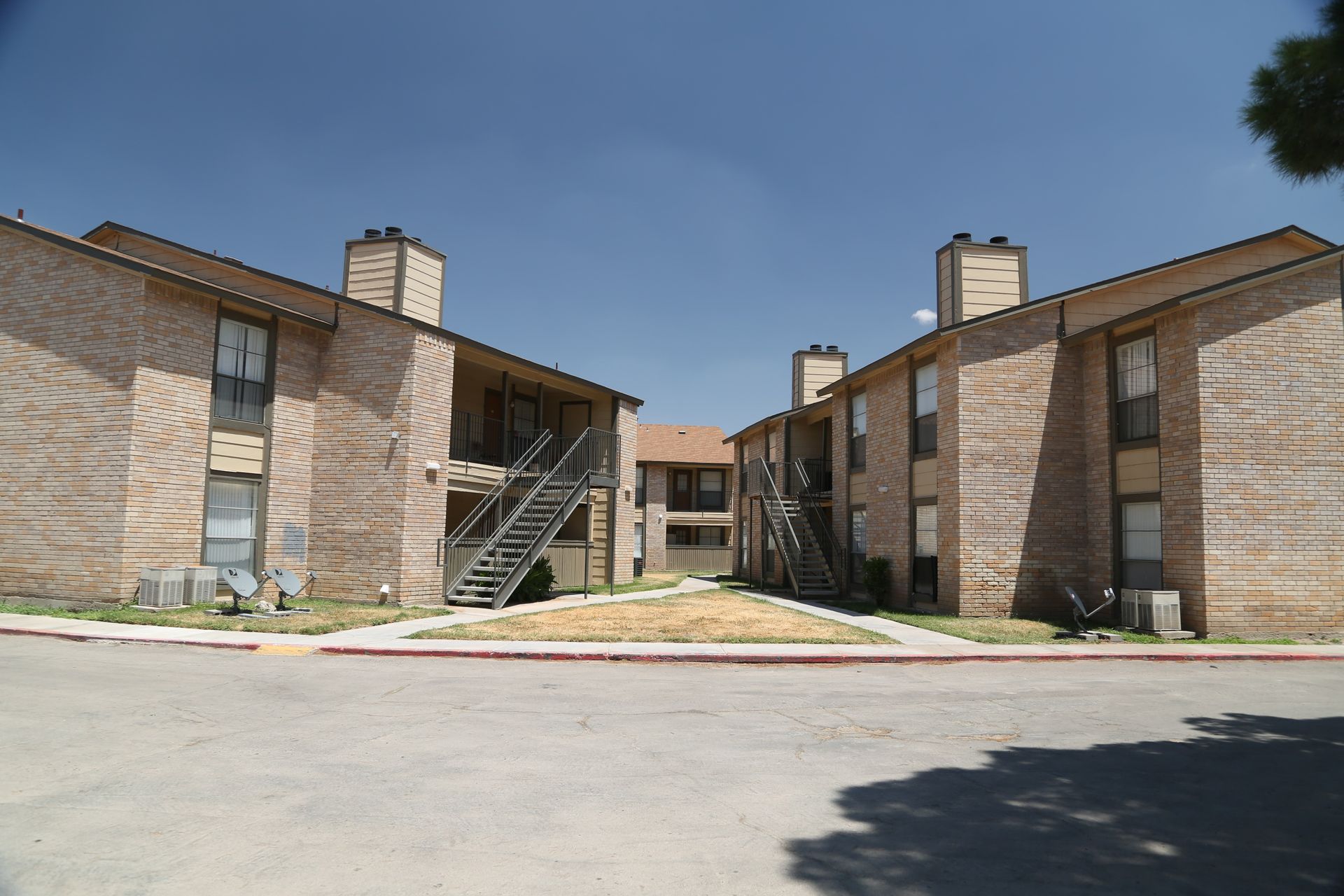 Apartment buildings, two-story, brick exteriors, clear sky. Parking area in foreground.