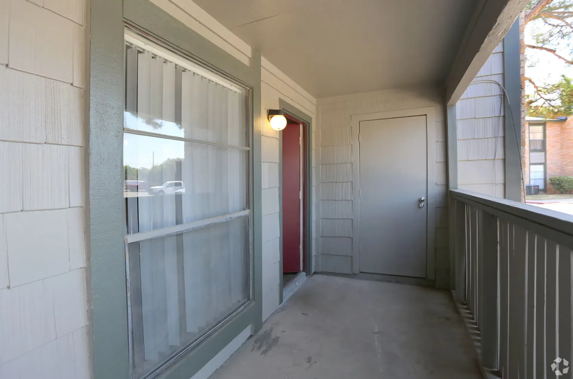 Exterior apartment walkway with a window, door, and railing on a shaded balcony at Woodview, offers apartments in Odessa, TX.