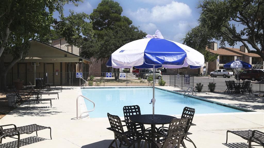 Outdoor community pool area with tables, chairs, and blue umbrellas at Woodview Apartment Homes in Odessa, TX.