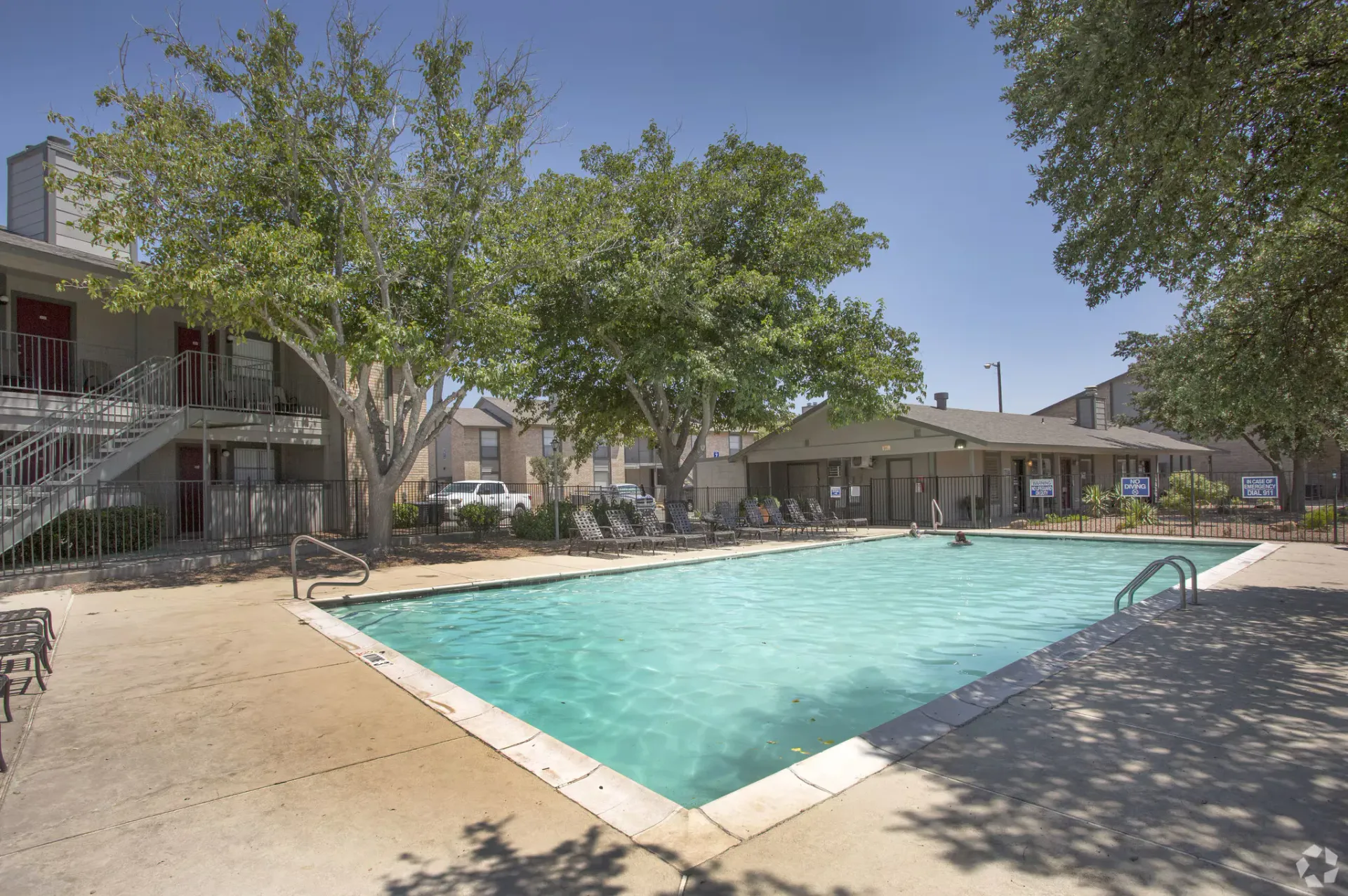 Outdoor pool at Woodview Apartment Homes in Odessa, TX, featuring lounge chairs and surrounding trees.