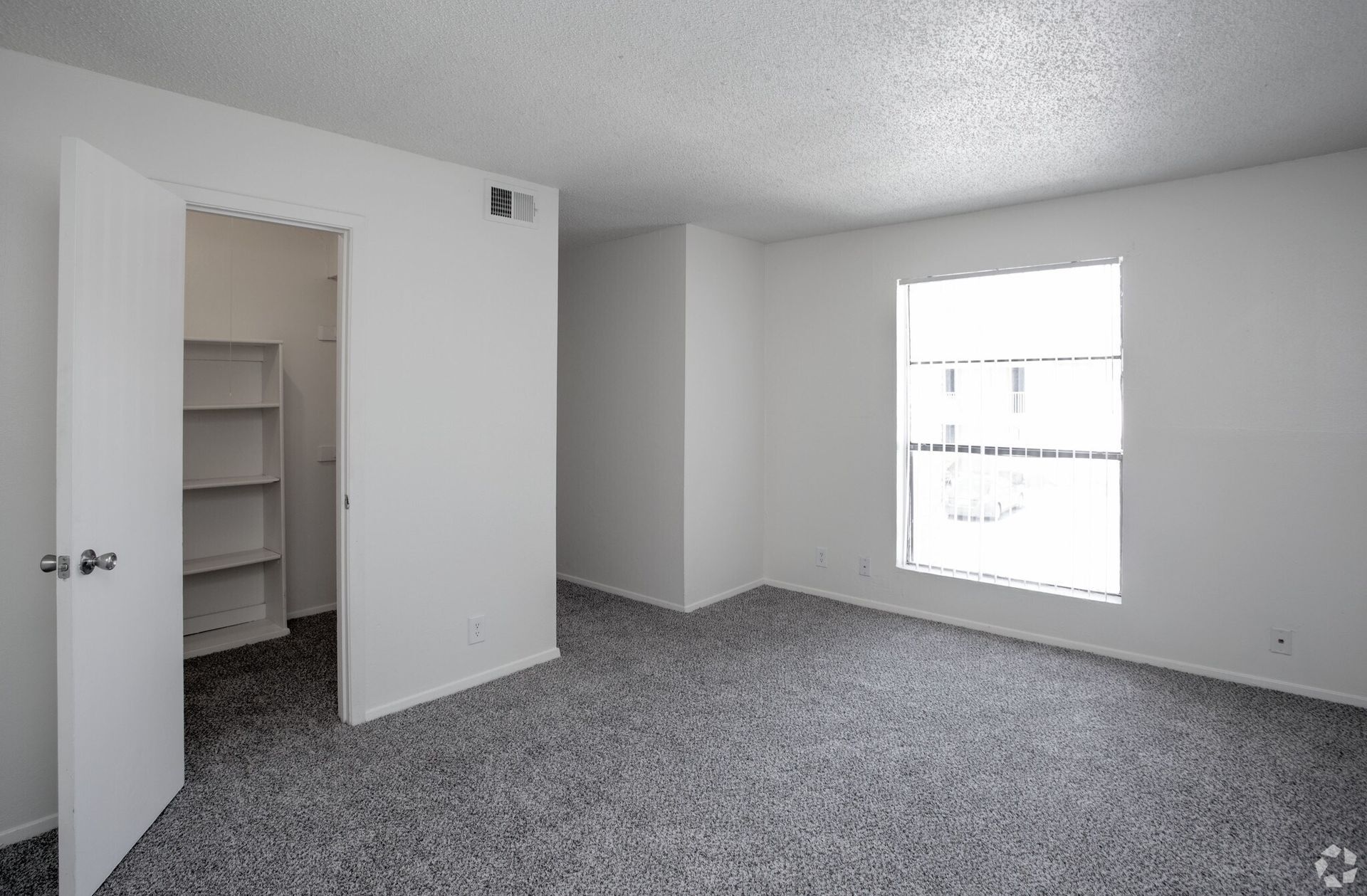 Empty apartment bedroom with white walls, carpet, built-in closet, and a window at Woodview, offers apartments for rent in Odessa, TX.