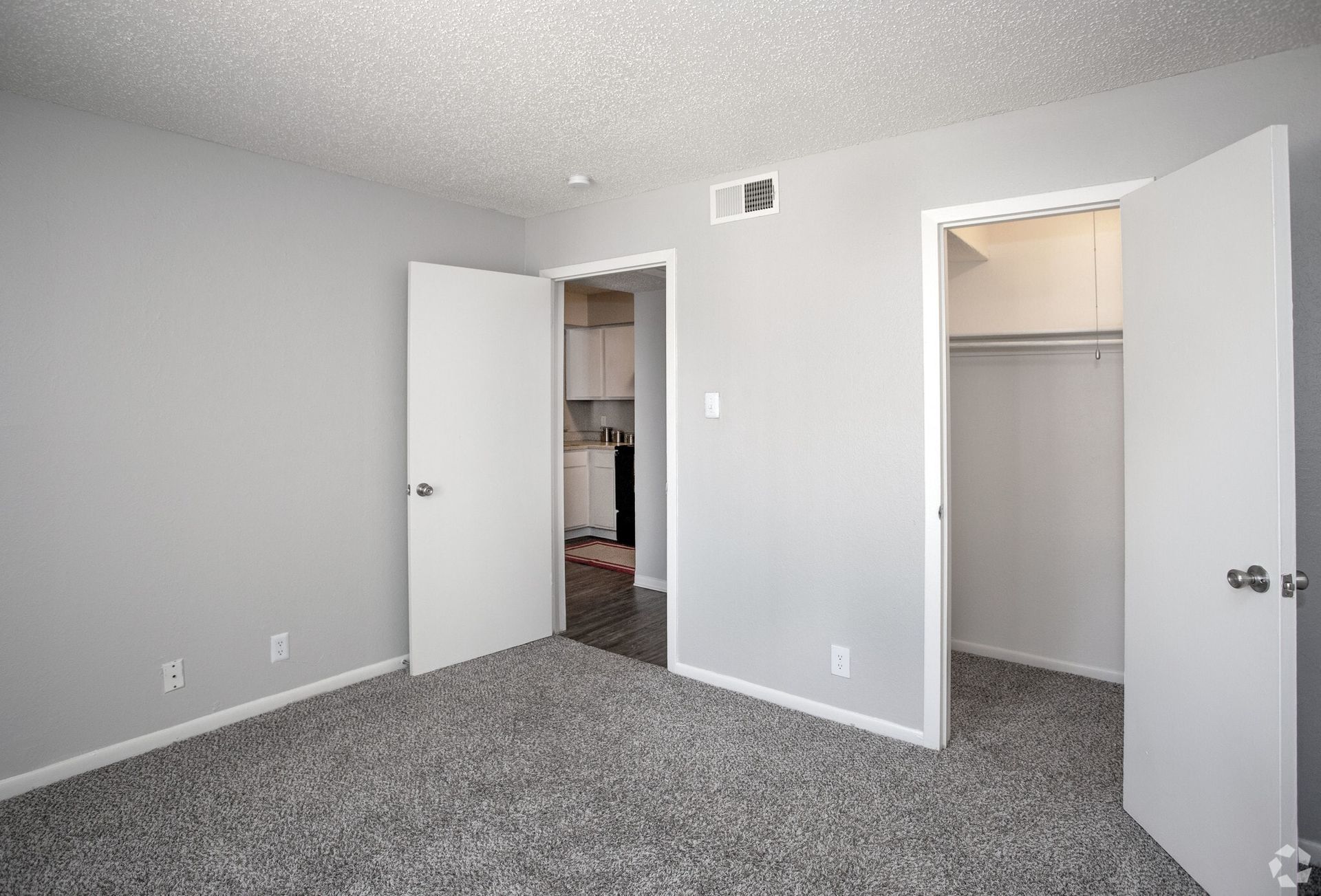 Bedroom in an apartment with gray walls, carpet, and two doors to kitchen and closet at Woodview, offers apartments for rent in Odessa, TX.