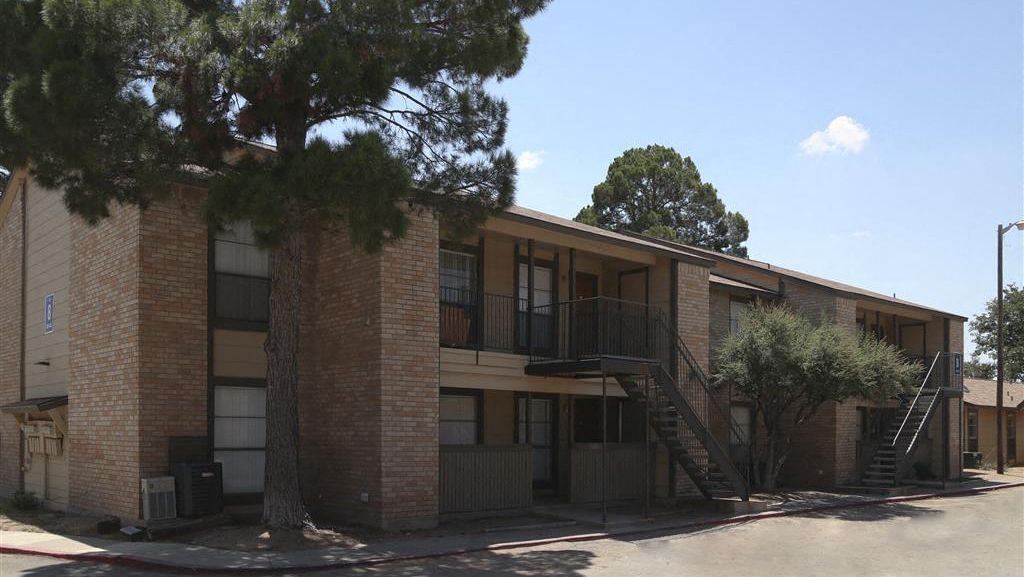 Two-story brick apartment building with external staircases and trees in front at Woodview, offers apartments in Odessa, TX.