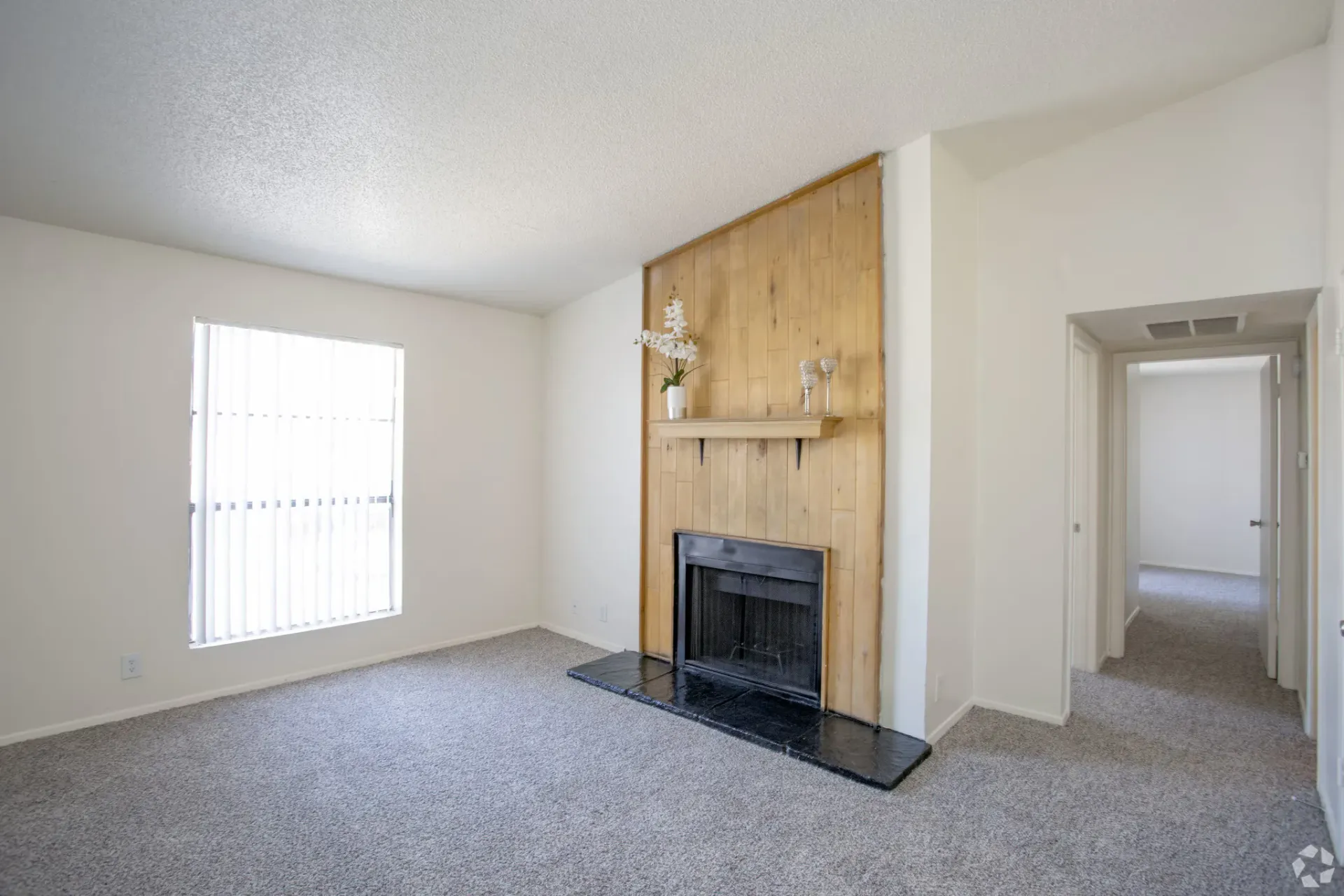 Living room with a wood-panel fireplace, white walls, and gray carpet at Woodview, offers apartments for rent in Odessa, TX.