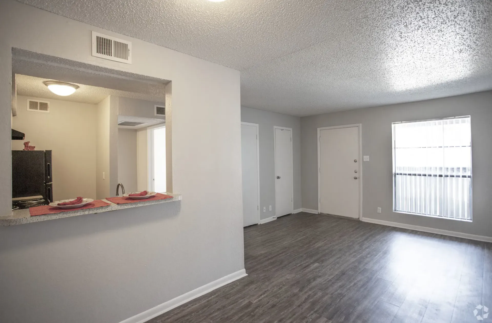 Open-concept living area with a kitchen pass-through, gray walls, and a large window at Woodview, offers apartments for rent in Odessa, TX.