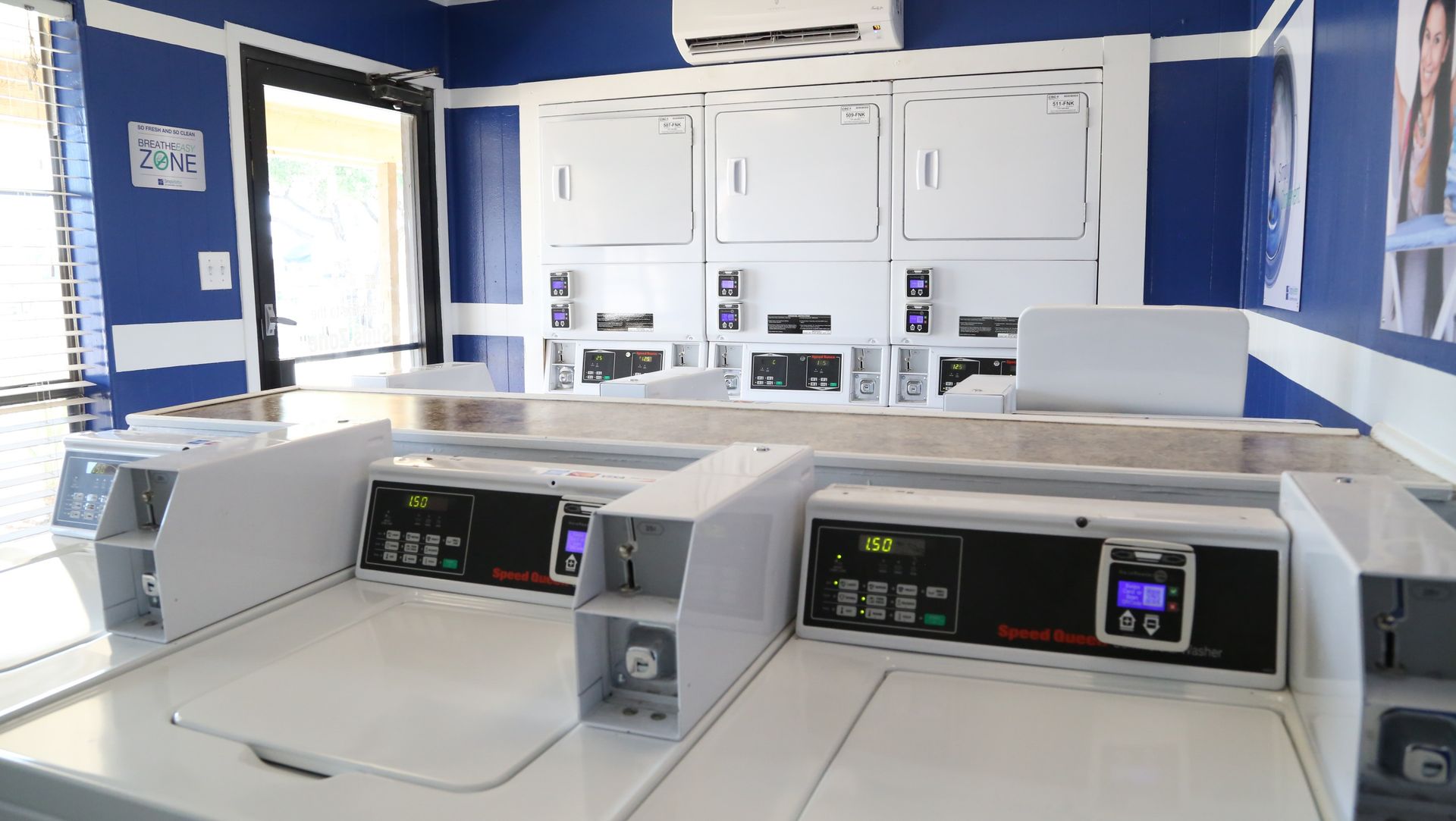 Laundromat-style laundry room with white coin-operated washers and dryers against blue walls at Woodview, offers apartments for rent in Odessa, TX.