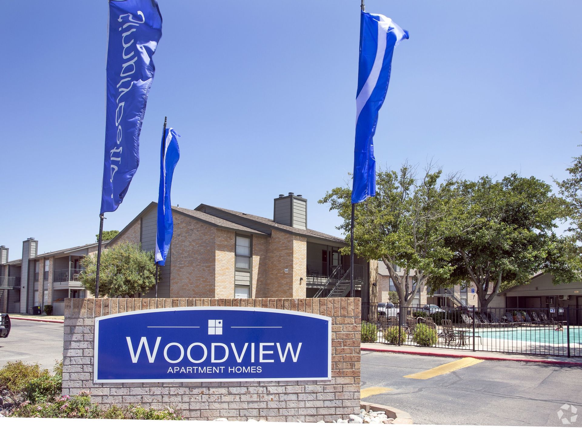 Exterior view of Woodview Apartment Homes with the entrance sign and pool area.