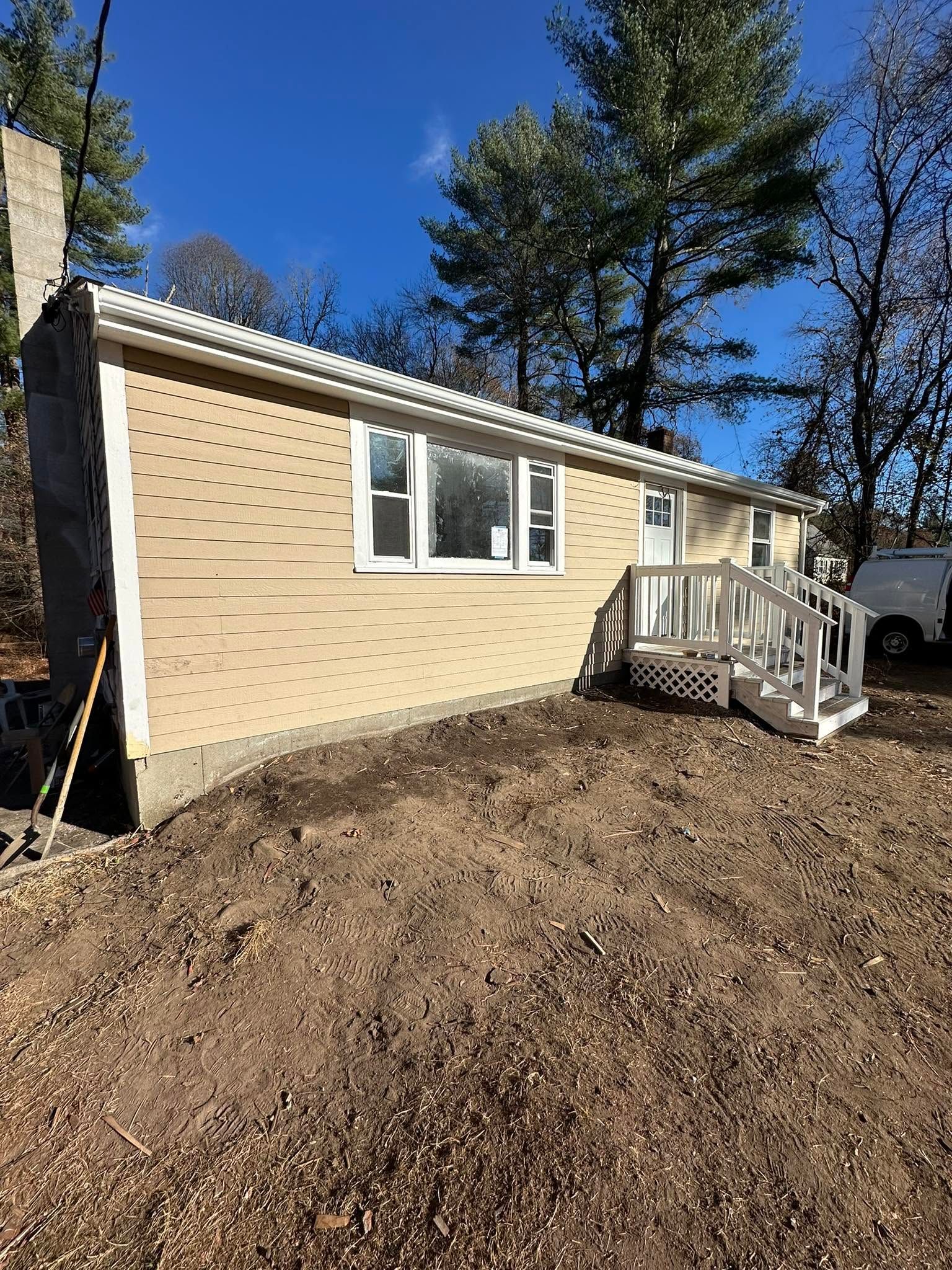 Single-story beige house with white trim and small front porch on a dirt yard under a blue sky