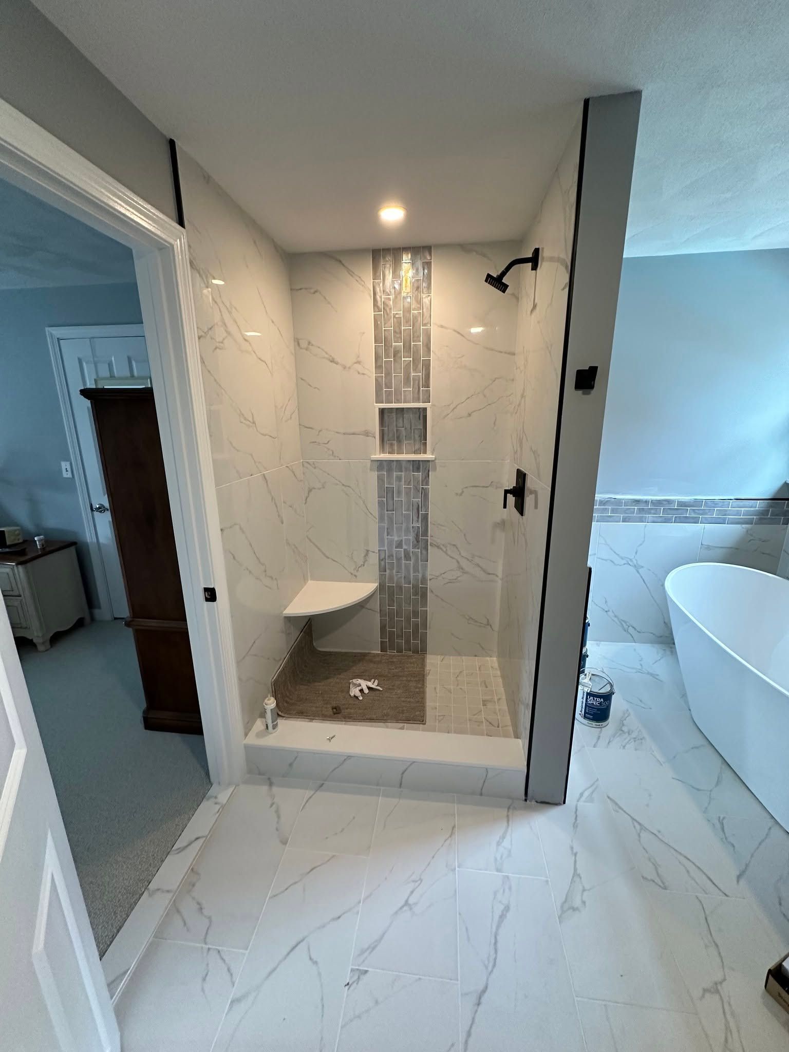 Modern bathroom with a tiled walk-in shower, glass panel, and white marble-style floor tiles.