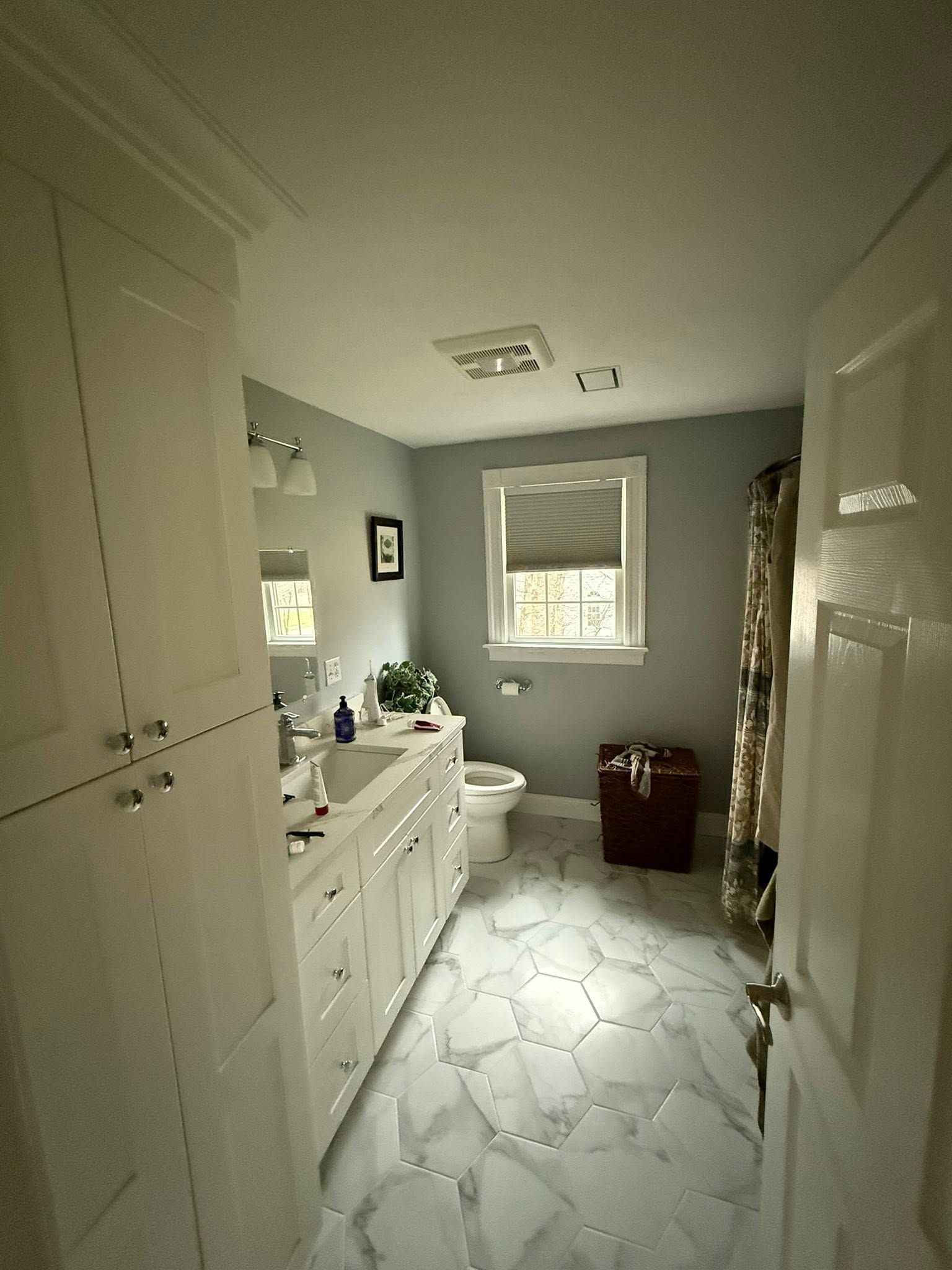 Bright bathroom with white cabinets, marble tile floor, toilet, and window.