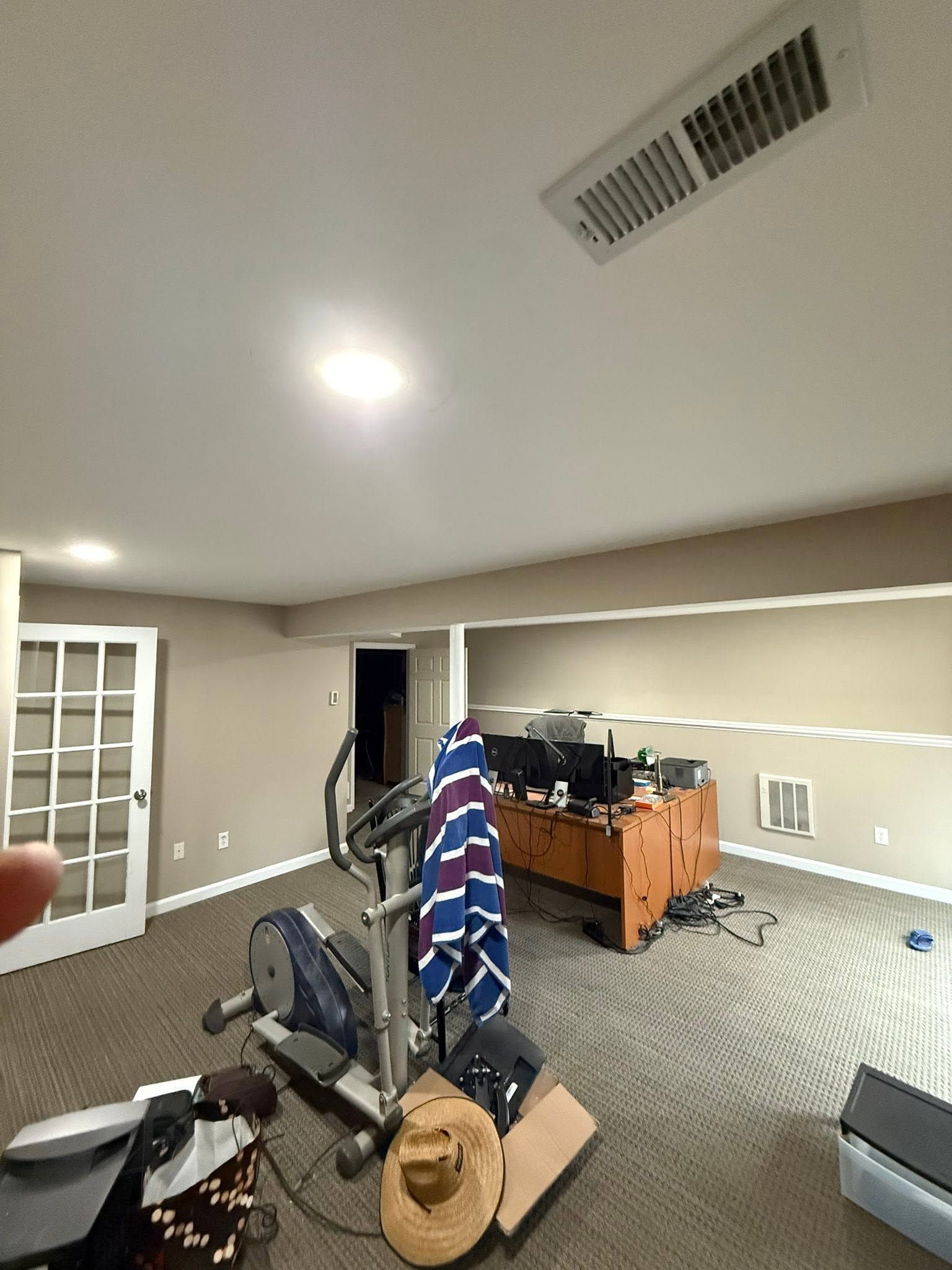 Cluttered home office with treadmill, desk, chair, cardboard boxes, and a blue-striped blanket draped over equipment
