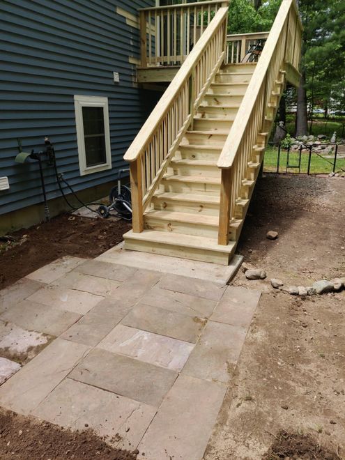 Wooden outdoor staircase beside a dark blue house, leading from a patio to an upper deck.