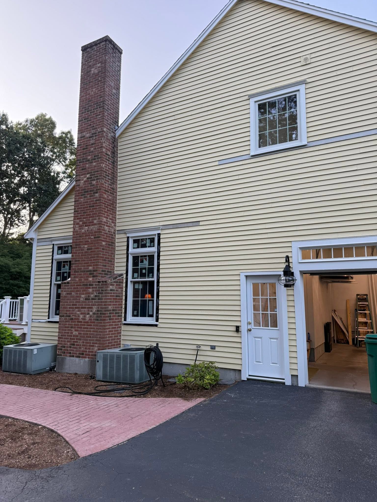 Yellow clapboard house with brick chimney, open garage door, and pink walkway.