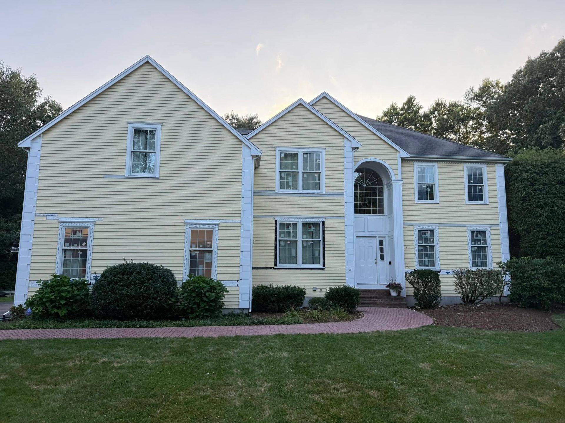 Large yellow two-story house with white trim, arched front entry, and a brick walkway in front