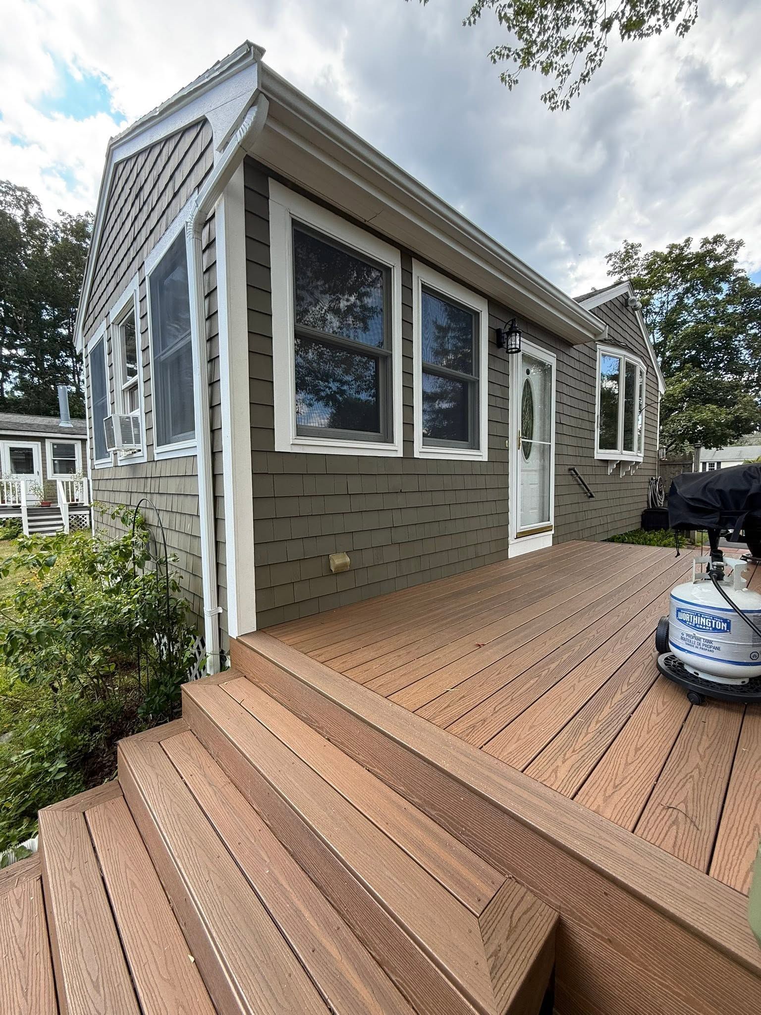 Wooden deck and steps beside a gray house with large windows, white trim, and a small outdoor seating area
