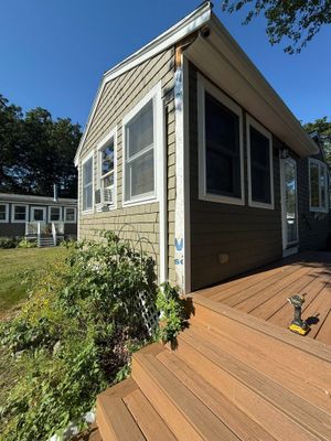 House exterior with tan siding, screened windows, and wooden steps under a blue sky