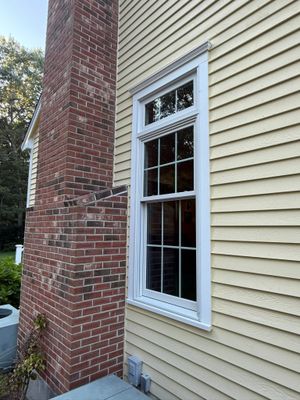 Brick chimney beside beige siding with a white-trimmed window on a house exterior