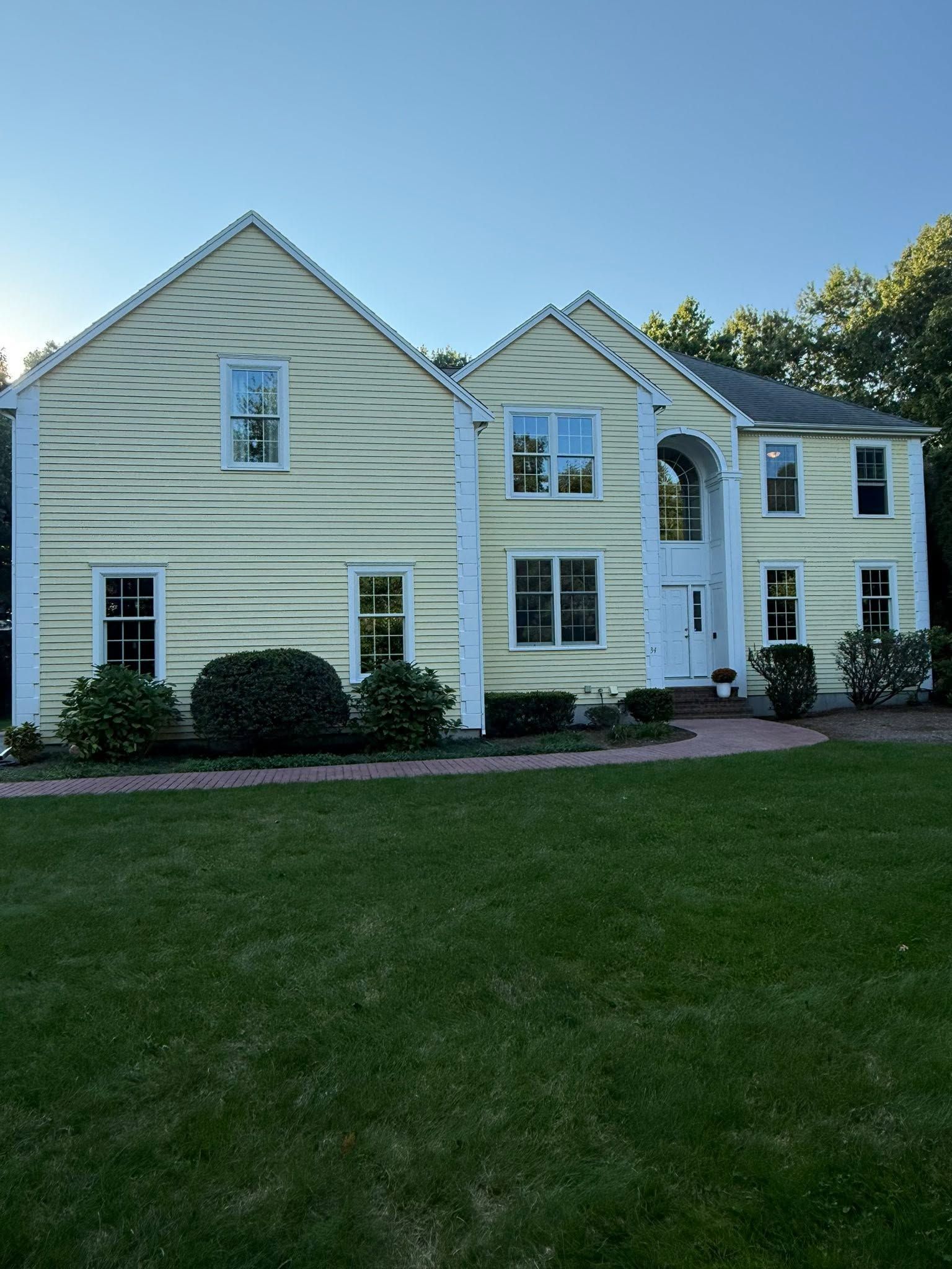 White two-story house with pale siding and a large green lawn under a clear blue sky