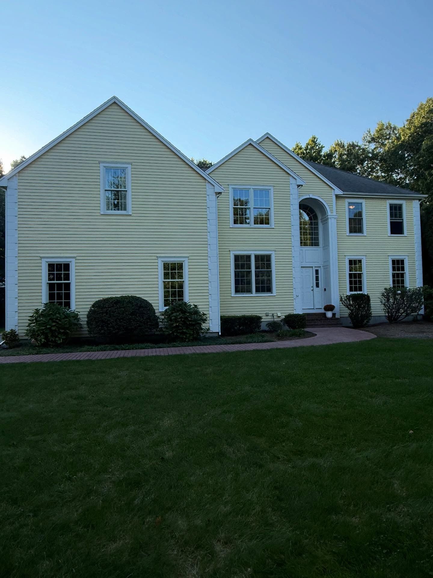 Two-story pale yellow house with white trim and a large green lawn under a clear blue sky