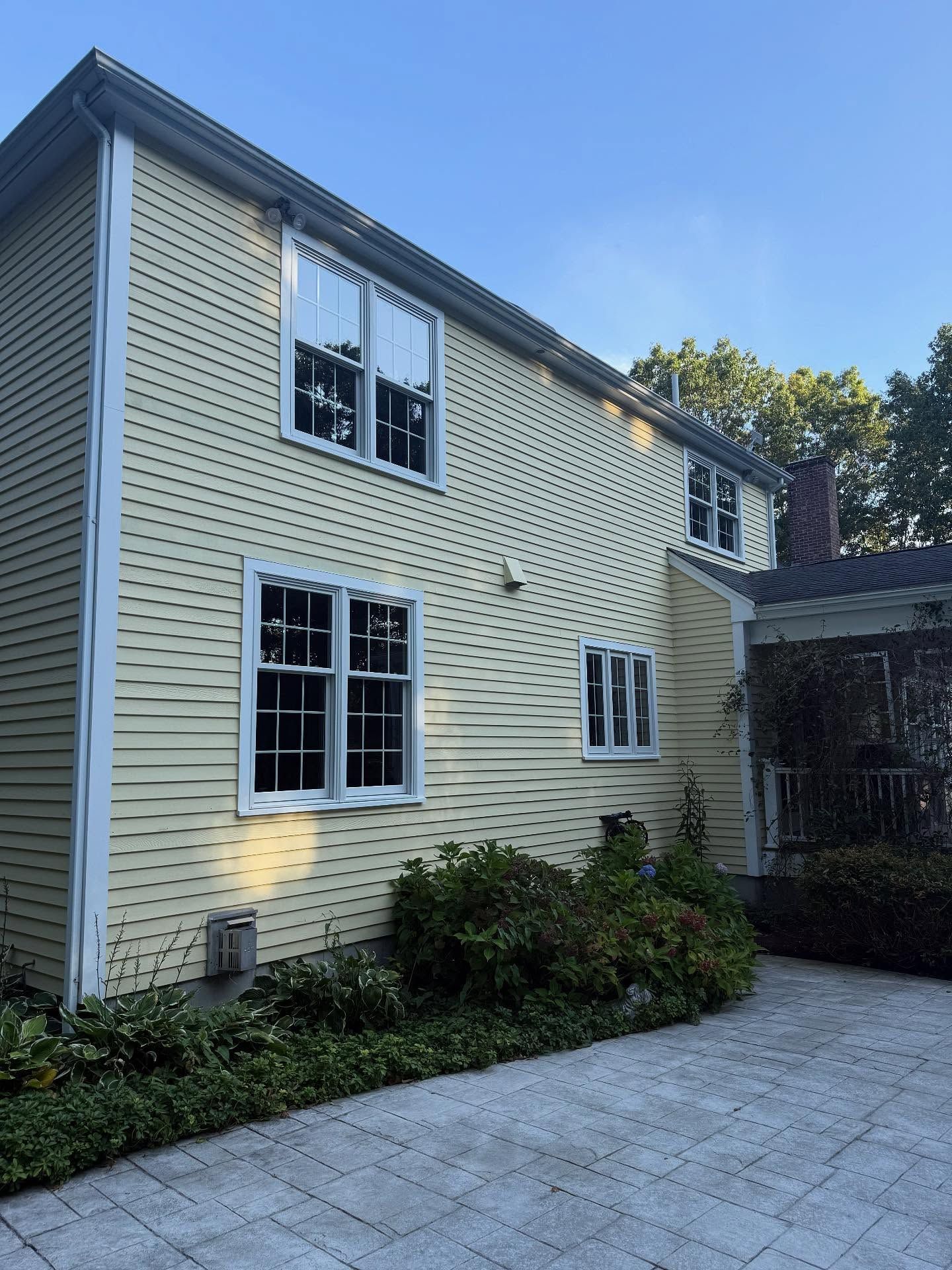 Two-story yellow house with white trim and paved patio in front, seen from the side