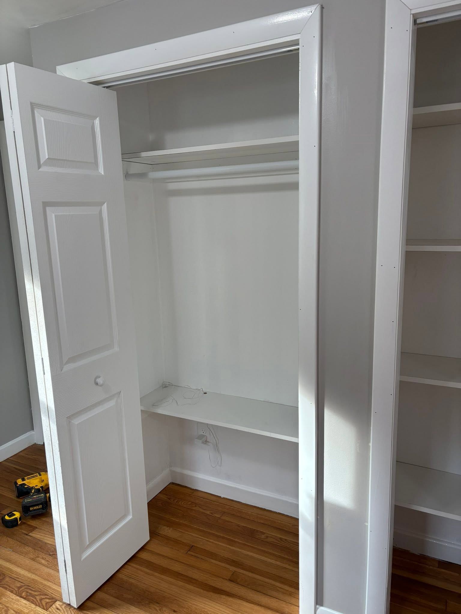 Open white closet with shelves and hanging rod, in a room with hardwood floor.