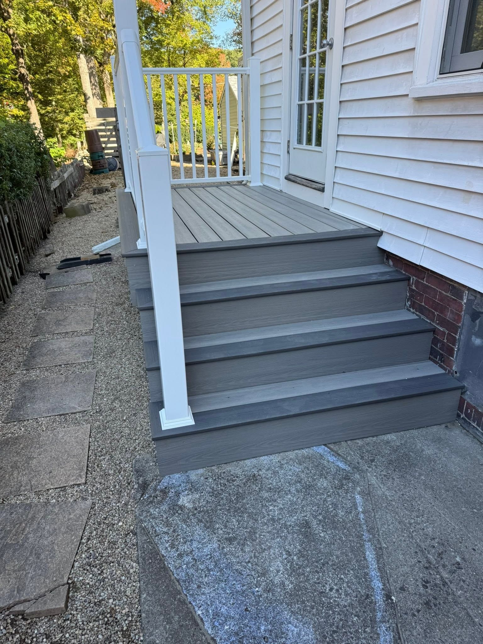 White wooden porch stairs with railing beside a house, leading from a gravel path.
