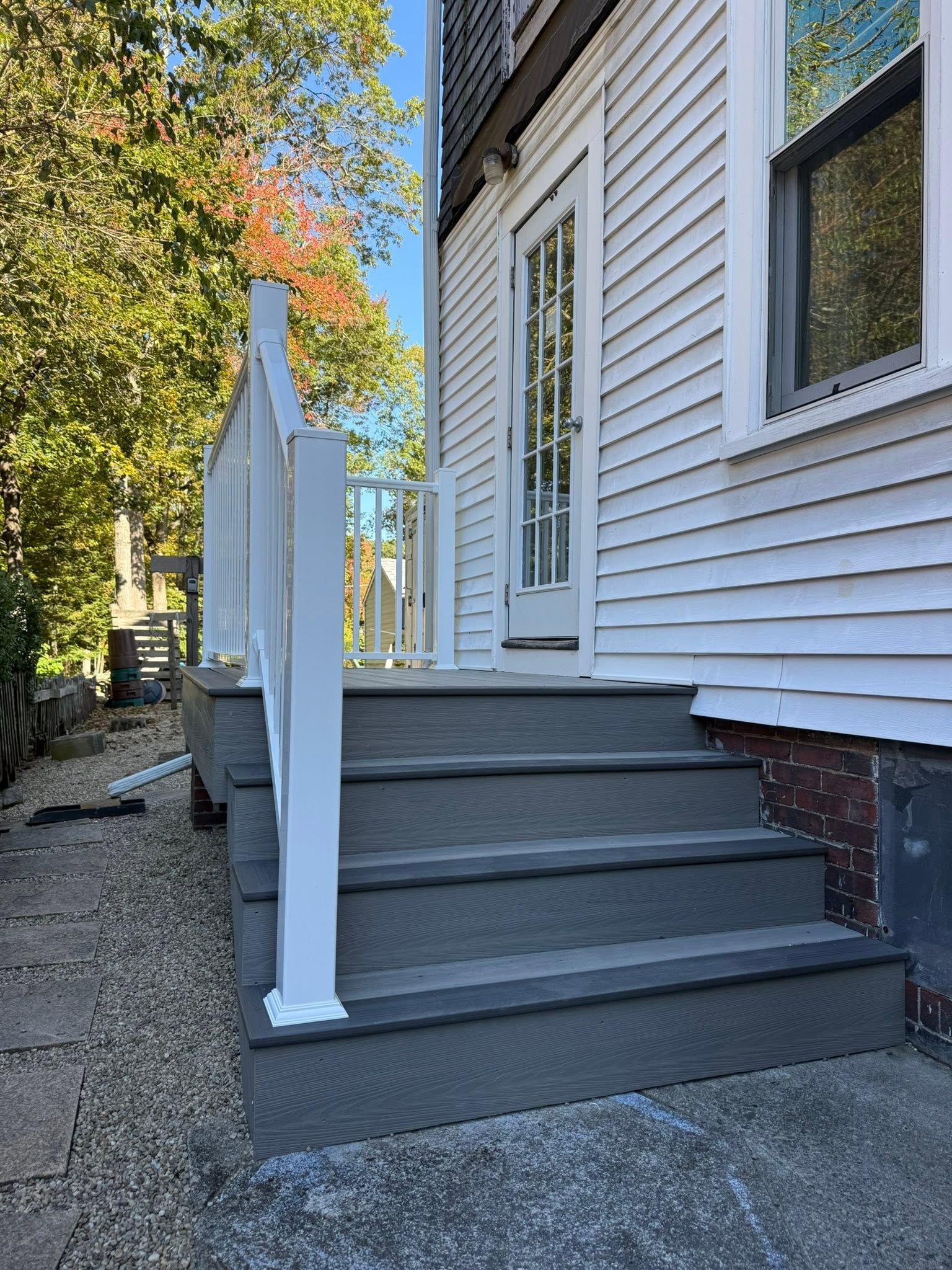 White house entry steps with a white railing and side door along a gravel path.
