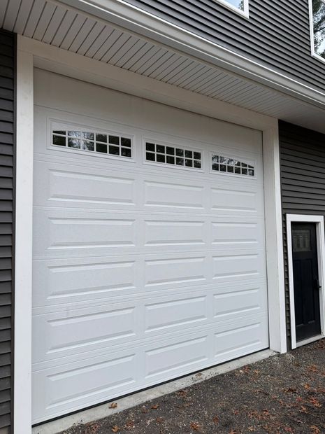 White garage door with decorative windows beside a house entrance and gravel driveway