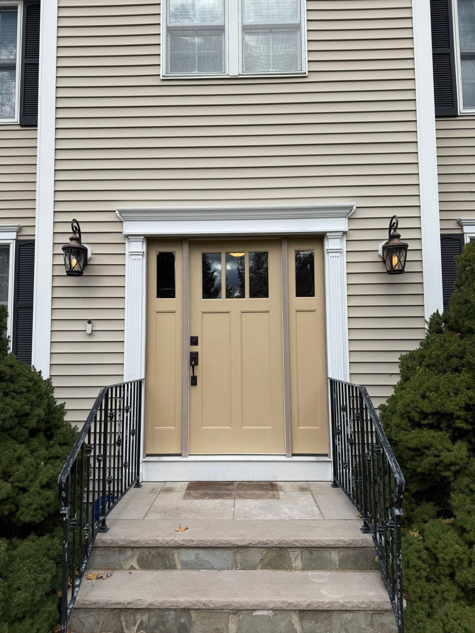 Front entrance of a beige townhouse with double doors, steps, black railings, and wall lanterns