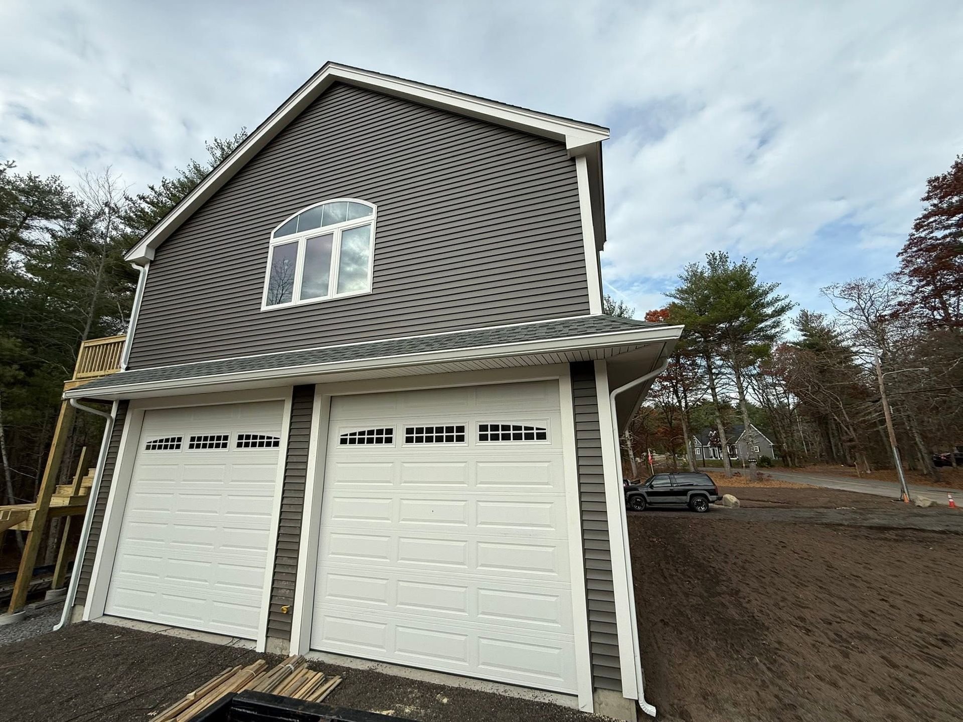 Two-story gray house with white garage doors and driveway under a cloudy sky