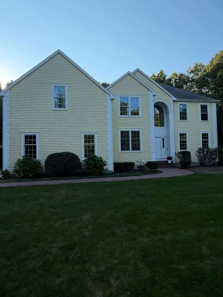 Large beige suburban house with white trim, arched entry, and a green lawn under a clear blue sky