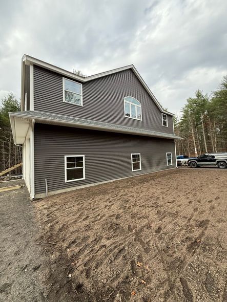 Modern dark-brown house with wavy roof siding on a mulched lot under cloudy sky