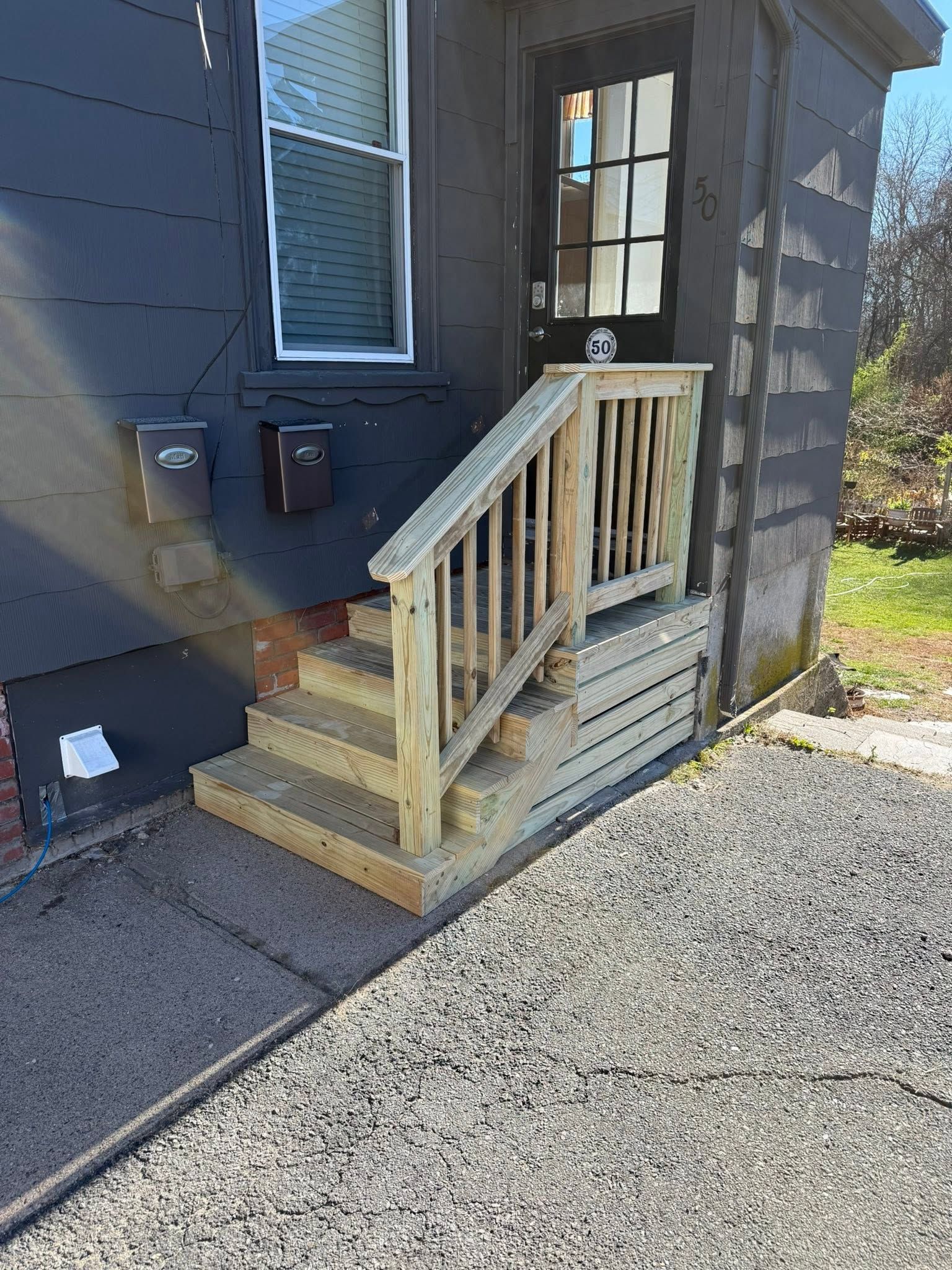 Small wooden wheelchair ramp with railings leading to a dark blue house entry door.