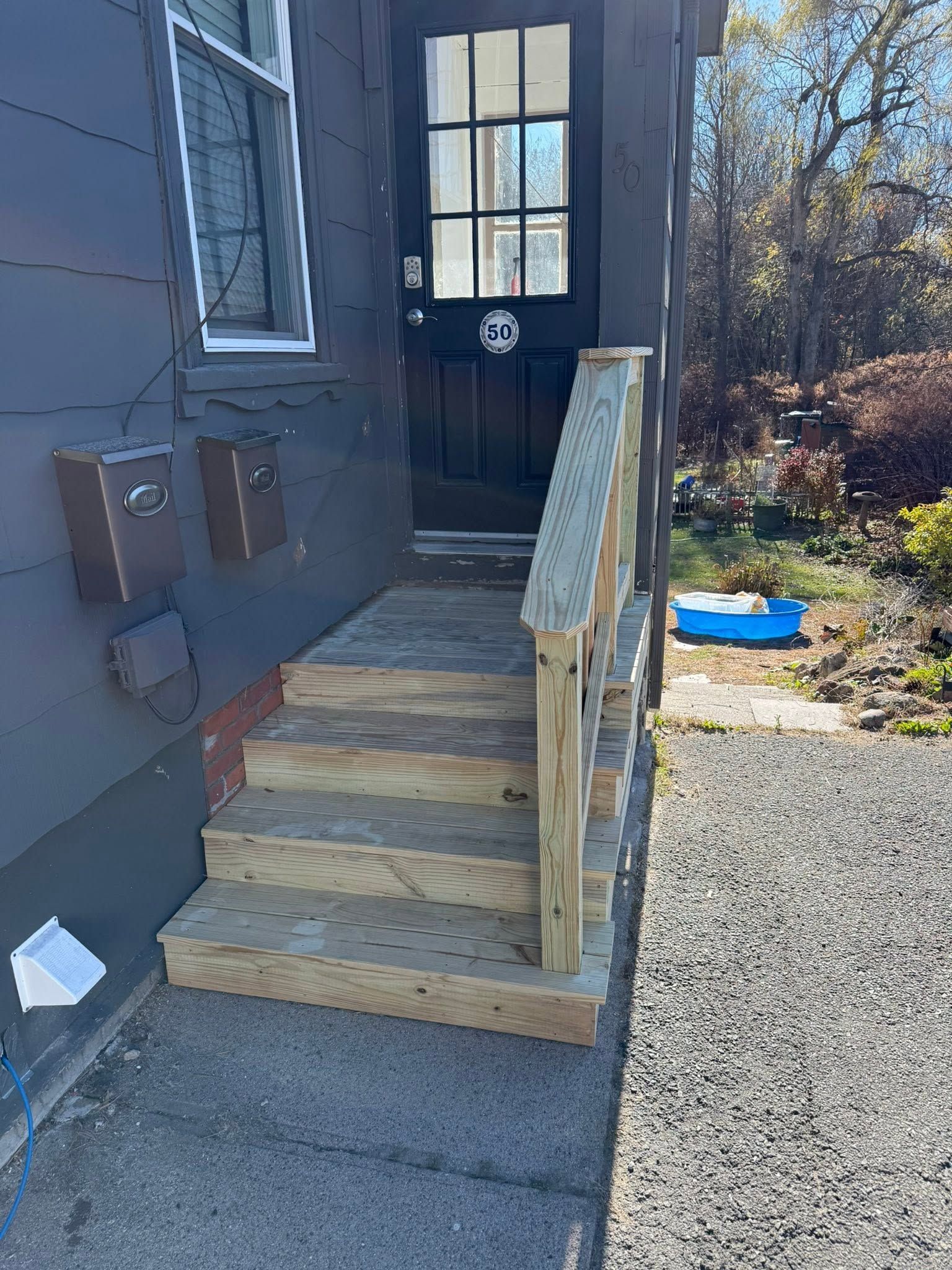 Wooden steps with handrails leading to a black door beside a gray house