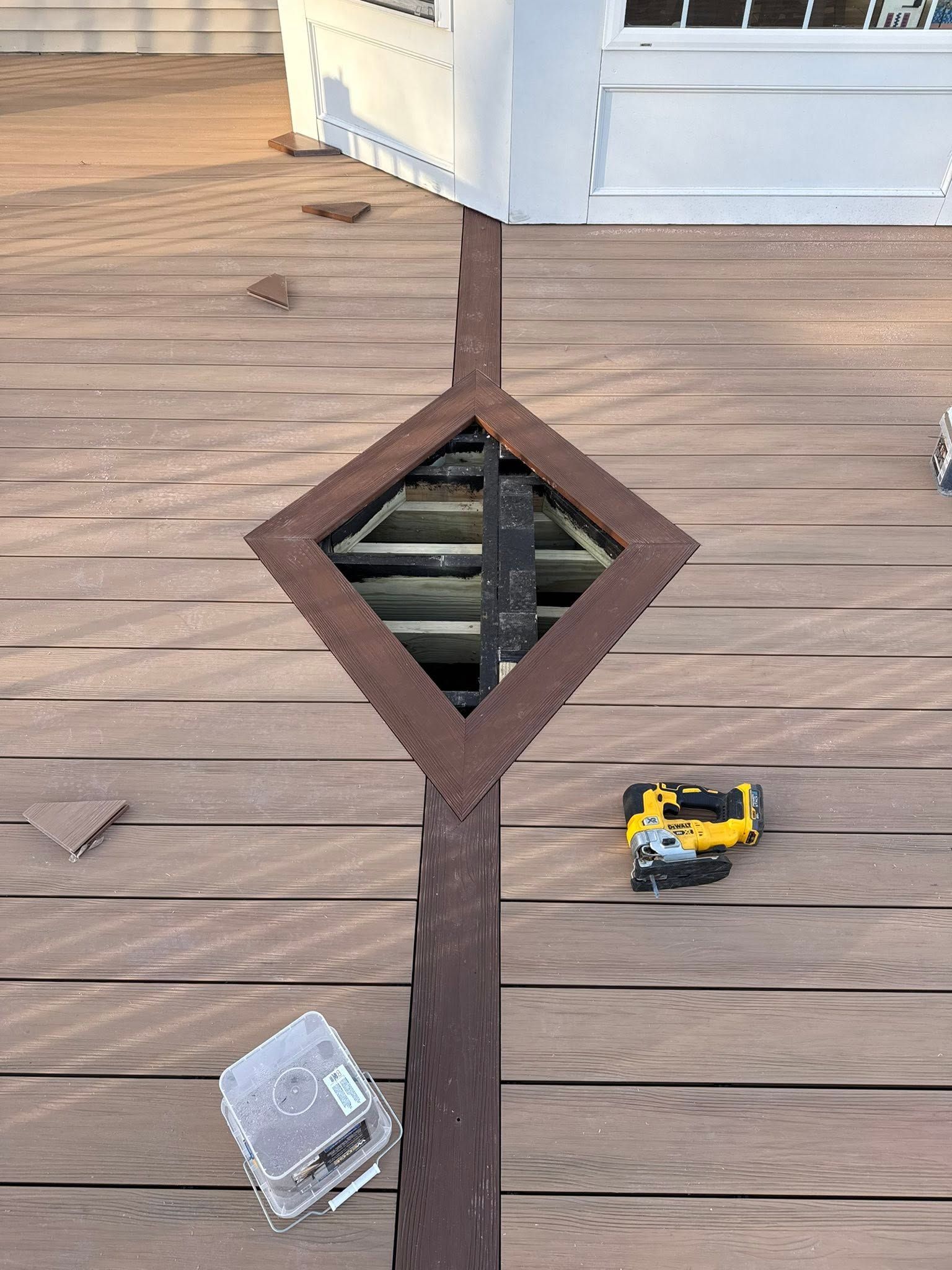 Wooden deck with a square opening, a yellow toy vehicle, and a clear plastic container nearby.