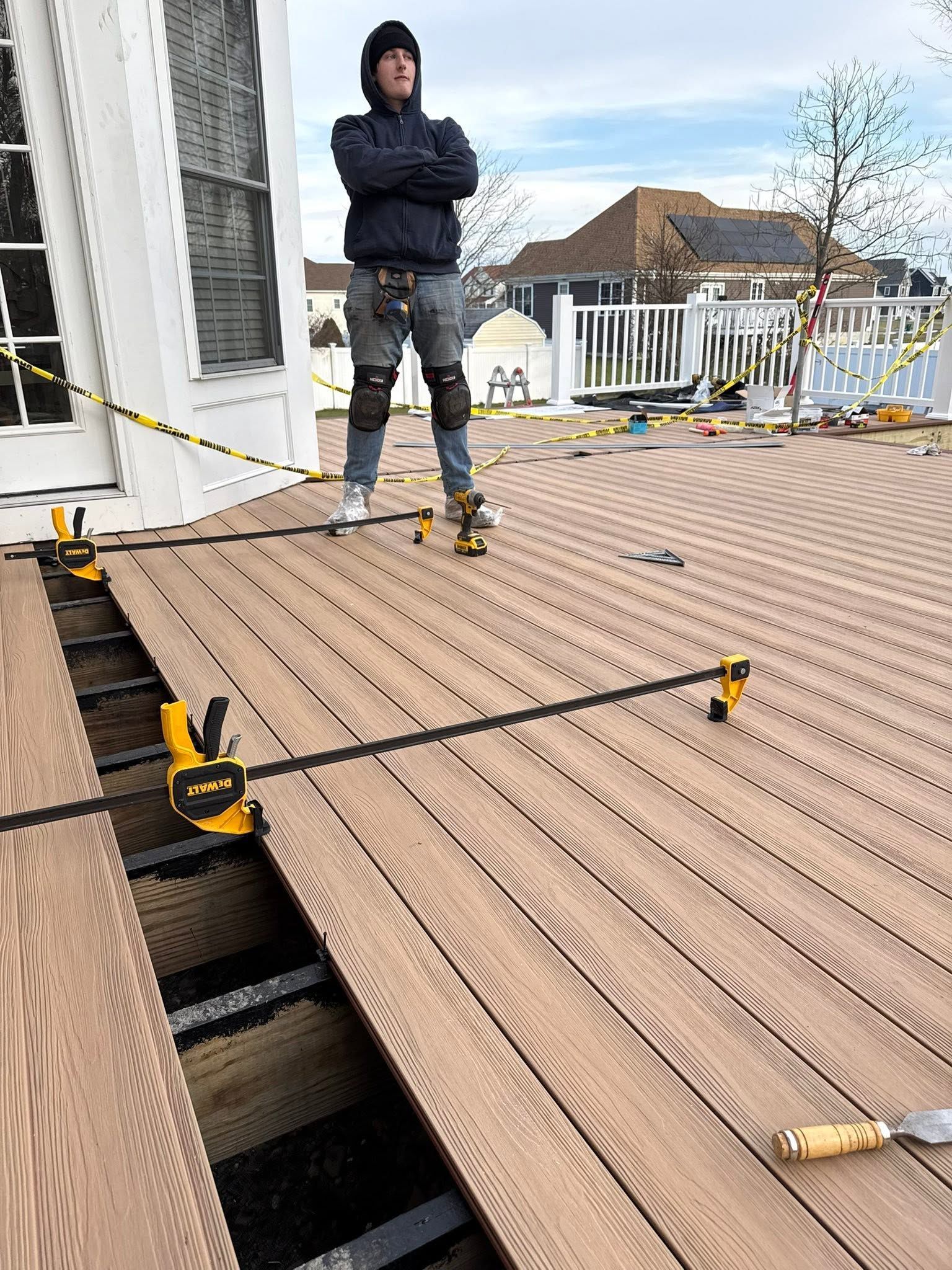 Worker standing on a rooftop deck under construction, with safety ropes and tools visible.