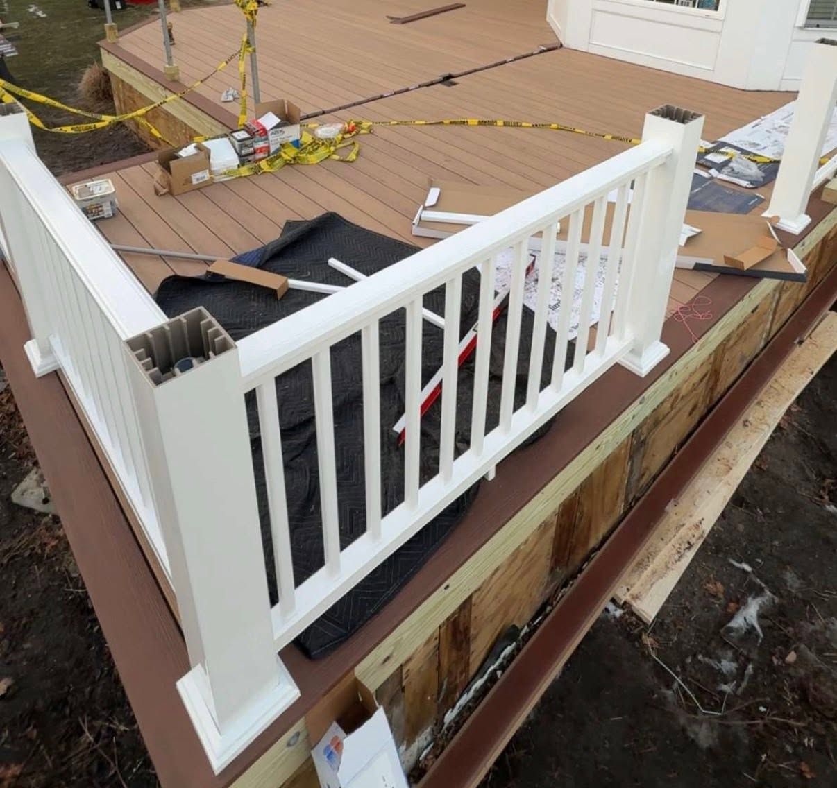 Damaged wooden deck with white railing and scattered debris, viewed from above