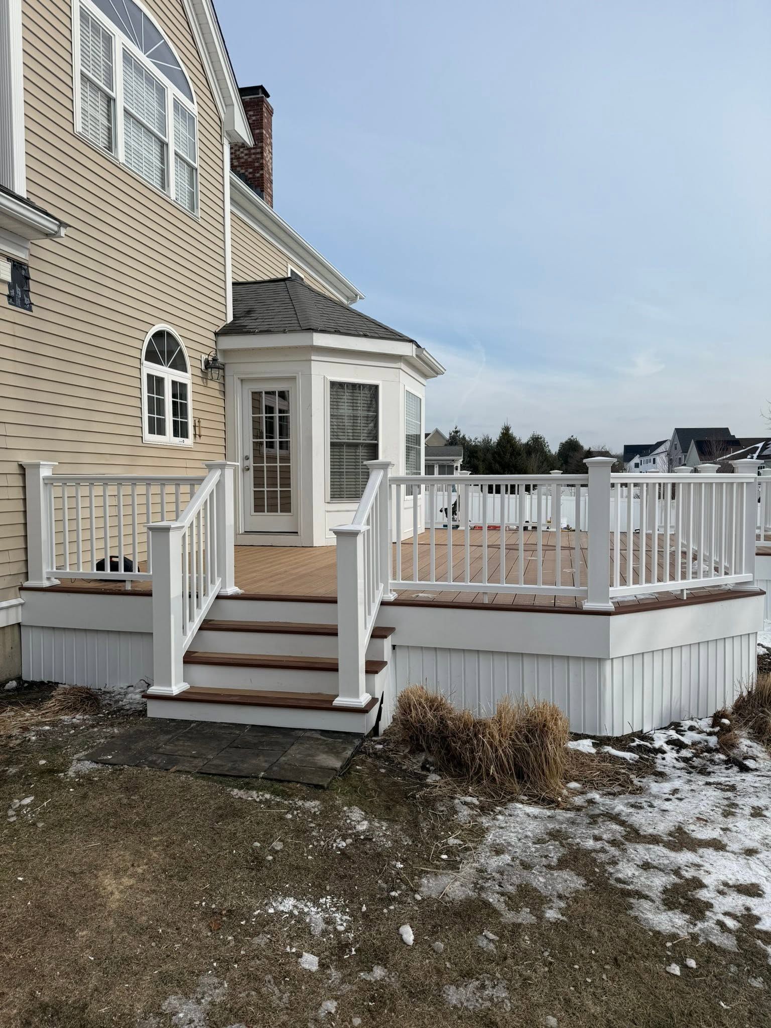 Backyard deck with white railing, steps, and a small covered entry beside a beige house in winter.