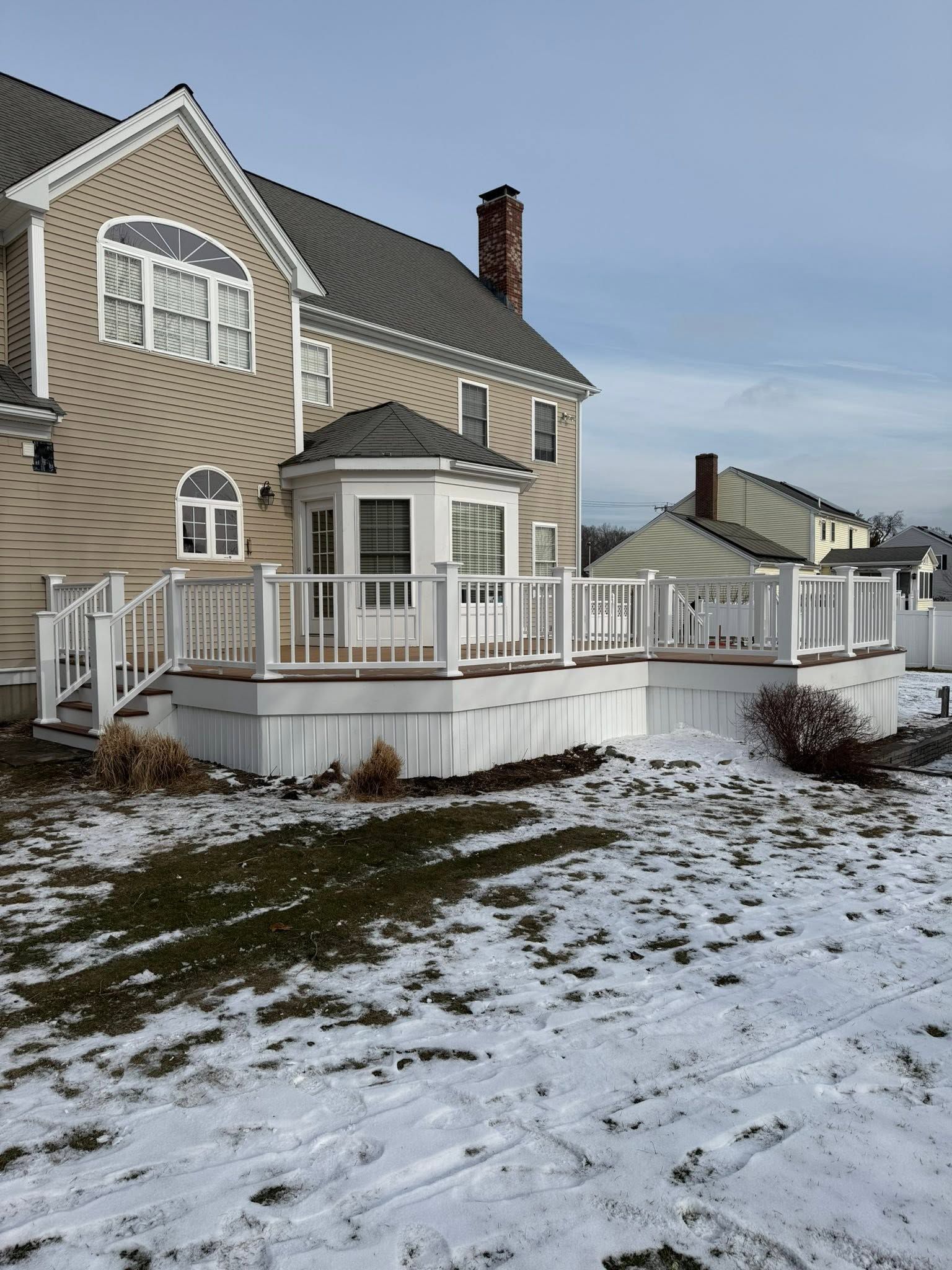 Snow-covered house with beige siding and white porch on a winter lawn