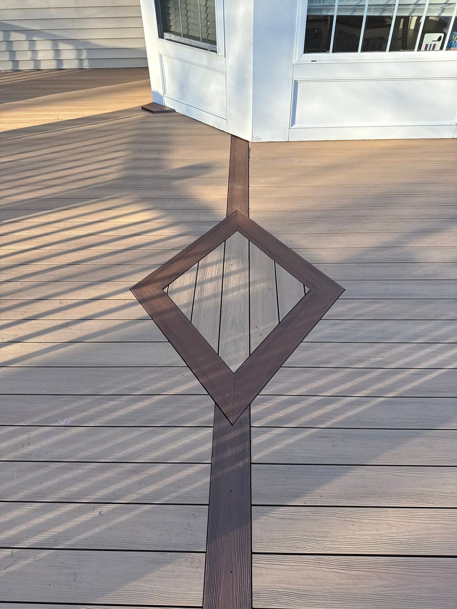 Brown wooden deck post with a diamond-shaped railing opening against a sunlit boardwalk.