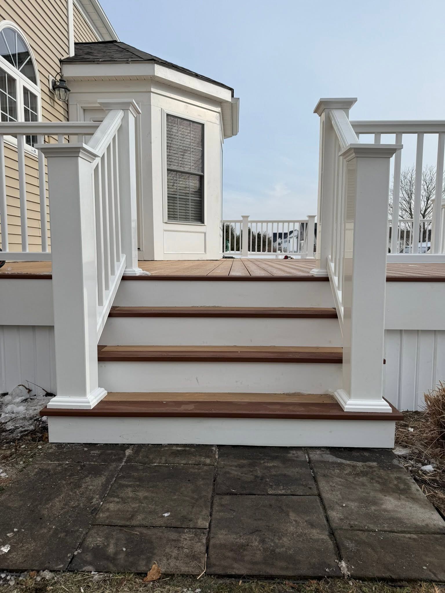 White deck stairs with railing leading to a small porch beside a house