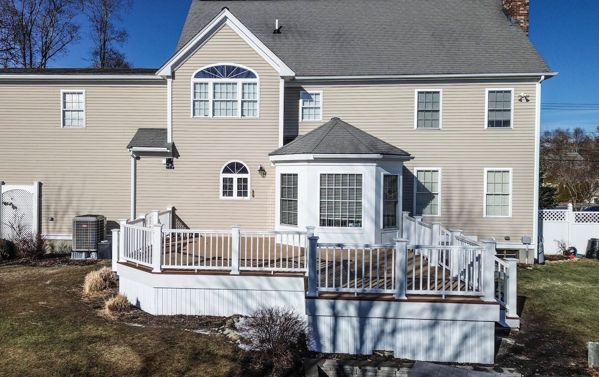 Suburban beige house with white deck and railing under a clear blue sky